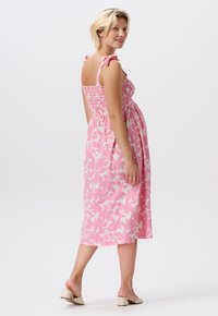 Rosa Midikleid mit weißem Blumenmuster, gerafftem Oberteil und Bindebändern. Glattes Material, A-Linie Silhouette und knielange Länge.