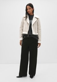 Kurtka z owczej wełny w jasnym kremowym kolorze z kołnierzem, w połączeniu z grafitowym dresowym swetrem i czarnymi spodniami o szerokich nogawkach. Szpiczaste czarne buty.