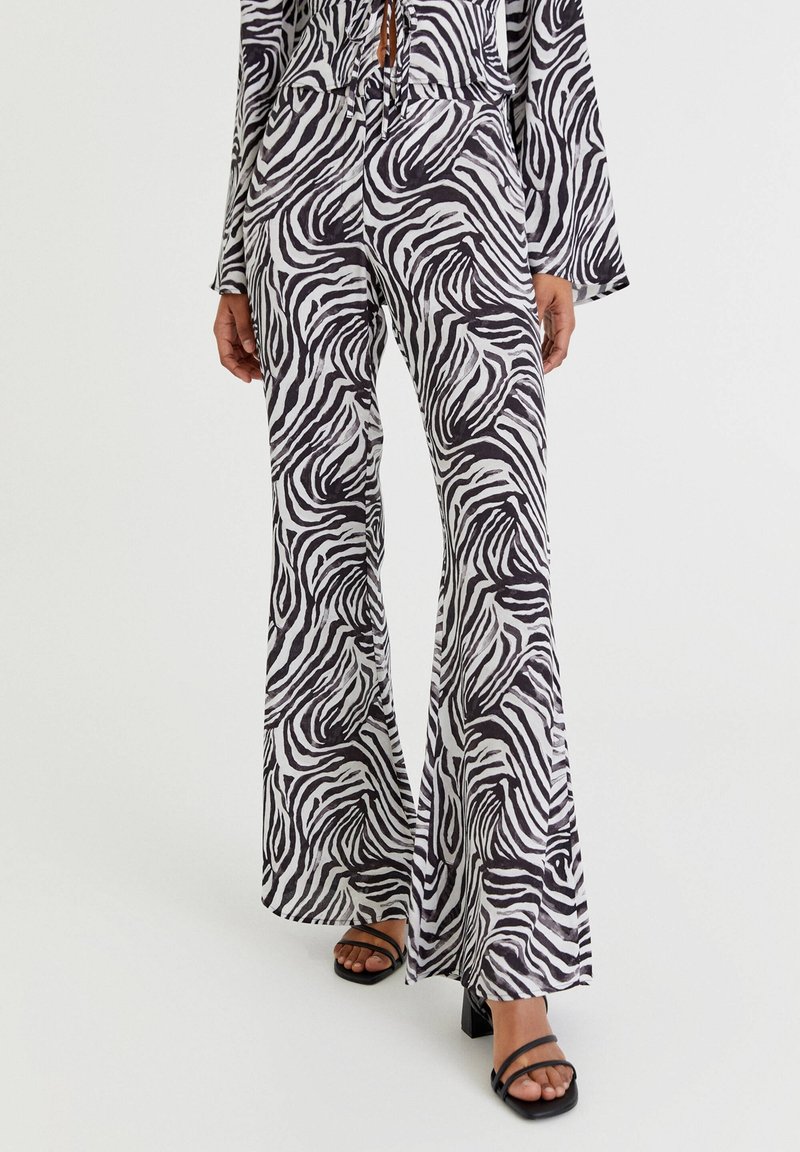Zwart-witte zebra print flared broek gemaakt van zacht materiaal, met een hoge taille en een ontspannen pasvorm, gecombineerd met zwarte sandalen met bandjes.