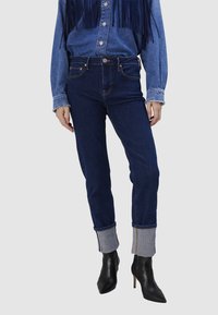 Jeans taille haute bleu foncé avec une silhouette ajustée et un ourlet retroussé. Les retroussages présentent un accent en denim clair avec des détails de couture.
