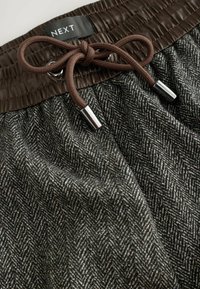 Gray and brown houndstooth patterned shorts with a textured elastic waistband, featuring a brown drawstring and silver metal tips.