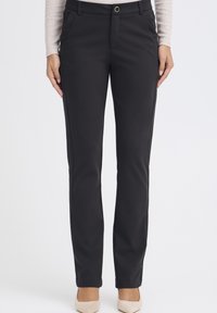 Černé kalhoty na míru s hladkou látkou, rovný střih, přední kapsy a zlatý knoflík v pase jako zdobný prvek.