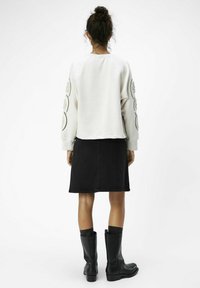 Witte sweatshirt met versierde mouwen, gecombineerd met een zwarte denimrok en zwarte laarzen tot de knie. Glad materiaal en getailleerd ontwerp.