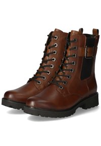 Bottes chelsea en cuir brun avec des lacets noirs, œillets en argent et un panneau élastique sur le côté. Semelle noire épaisse avec un motif de semelle robuste.