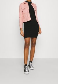 Chaqueta de mezclilla rosa, minivestido negro con costillas y zapatillas negras de caña alta. La chaqueta cuenta con cierre de botones y bolsillos, el vestido es ajustado.