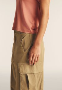 Top corta a maniche corte di colore rosa chiaro abbinato a pantaloni cargo beige, con tasche laterali e una tasca a pattina con dettaglio del logo. Tessuto liscio e traspirante.