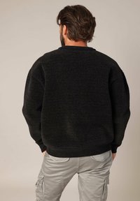 Pull noir surdimensionné avec une finition texturée, col rond et ourlet côtelé. Porte avec un pantalon cargo gris clair, vue de dos.