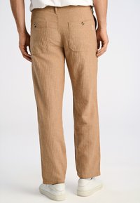 Ljust bruna, texturerade byxor med två bakfickor och kontrasterande sömmar, med en rak bendesign och subtila vertikala ränder.