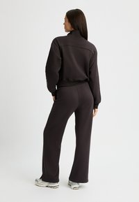 Sudadera negra ajustada con cuello alto, combinada con pantalones de chándal de pierna ancha. El material parece suave. Presenta una textura lisa y un diseño minimalista.