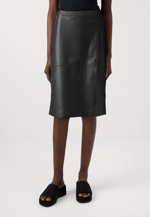 Falda de cuero negra con un diseño elegante, de longitud media, que presenta una textura suave y detalles de costura sutiles. Combinada con sandalias de plataforma negras.