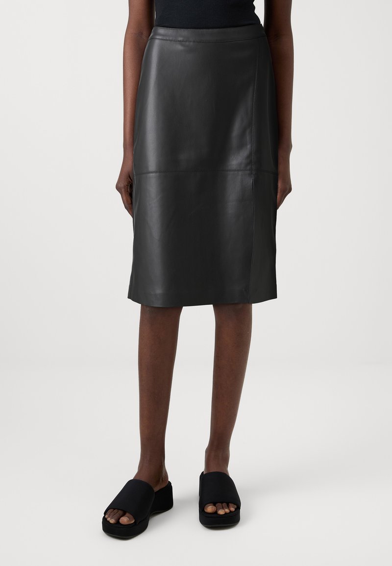 Jupe en cuir noir au design épuré, mi-longue, dotée d'une texture lisse et de détails de couture subtils. Associée à des sandales à plateforme noires.