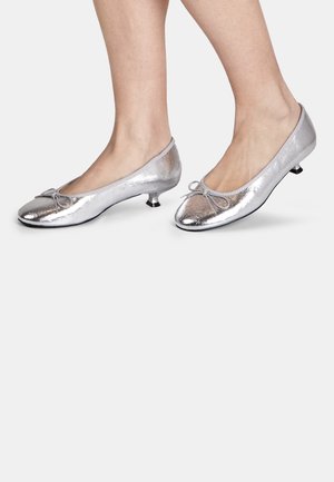 Ballerine piatte metallizzate argento con punta arrotondata, dettaglio di piccolo fiocco, tacco basso e materiale superiore dalla texture liscia.