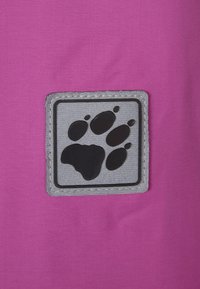 Rosa tyg med en strukturerad yta som har en grå fyrkantig lapptäck som visar ett svart tassavtryck i mitten.