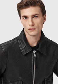 Sort læderjakke med krave, lynlås foran og to forlommer. Glat tekstur med synlige syningsdetaljer.