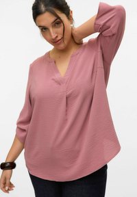 Blusa a scollo a V ampia in morbido tessuto rosa testurizzato. Caratterizzata da maniche a tre quarti e una silhouette rilassata, abbinata a jeans scuri.