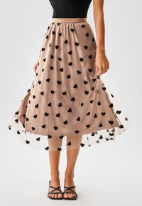 Cremefarbener Midirock mit schwarzen Herzmustern, elastischem Bund und transparentem Überzug. Kombiniert mit schwarzen Riemchensandalen.