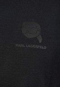 Černé tričko s vystouplým tónovaným potiskem obličeje s brýlemi a textem "KARL LAGERFELD" dole, vyrobené z hladké látky.
