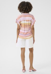 Top leggero a maniche corte con un motivo a righe orizzontali multicolori in rosa, arancione e lavanda; indossato con pantaloni corti bianchi e mule con tacco rosa.