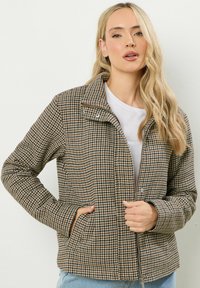 Giacca a motivi houndstooth in marrone e beige, con zip, due tasche anteriori e design con colletto, realizzata in tessuto testurizzato.