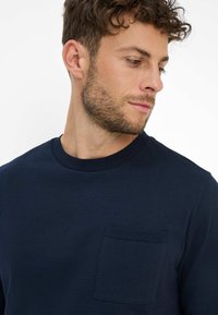 Marineblaues Baumwoll-Sweatshirt mit Rundhalsausschnitt, ausgestattet mit einer strukturierten Pattentasche auf der linken Brust und einer glatten Stoffoberfläche.