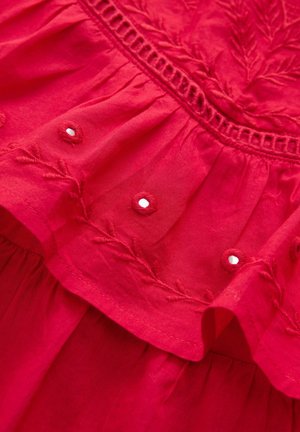 Tissu en coton rouge avec des motifs de feuilles brodés, ourlet volanté et boutons décoratifs. Texture lisse avec une apparence légère et aérée.