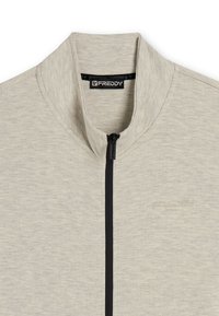 Giacca zip-up grigio chiaro con collo alto, zip nera e logo del brand in rilievo. Tessuto morbido e testurizzato con una finitura liscia.