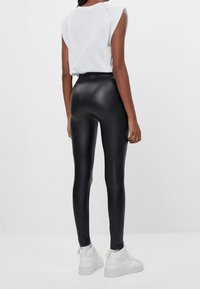 Svarta leggings i konstläder med hög midja, figurnära design och slät yta, ihop med en vit t-shirt med kort ärm och vita sneakers.