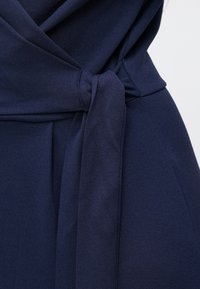 Detalle de vestido de tela azul marino con un lazo atado en la cintura, textura suave y diseño estructurado con drapeado frontal.