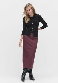 Cardigan noir en maille côtelée avec des boutons blancs, associé à une jupe crayon bordeaux et des bottes noires texturées jusqu'aux genoux.
