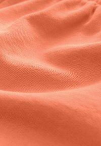 Korallenfarbener Stoff mit einer strukturierten, gerippten Oberfläche, der weiche Falten aufweist und so für wechselndes Licht und Schatten auf dem Material sorgt.