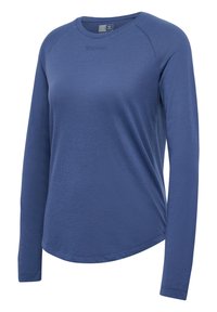 Niebieska bluzka z długim rękawem wykonana z fakturowanej tkaniny, z okrągłym dekoltem i subtelnym logo na wysokości klatki piersiowej. Góra ma zaokrąglony dół.
