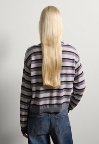 Suéter gris a rayas con franjas en color burdeos y marino, de diseño corto, con puños acanalados y un ajuste relajado, combinado con jeans de mezclilla azul.