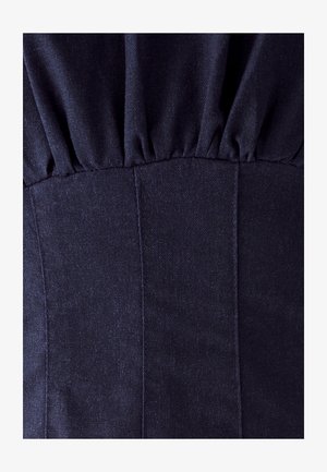 Mørkeblå stof med en tekstureret overflade, der har samlet detaljer øverst og lodrette sømme langs brystpartiet.