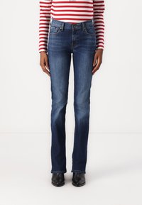 Blue denim jeans with a slim fit, flared leg, five-pocket design, and contrasting stitching. Worn with black ankle boots.