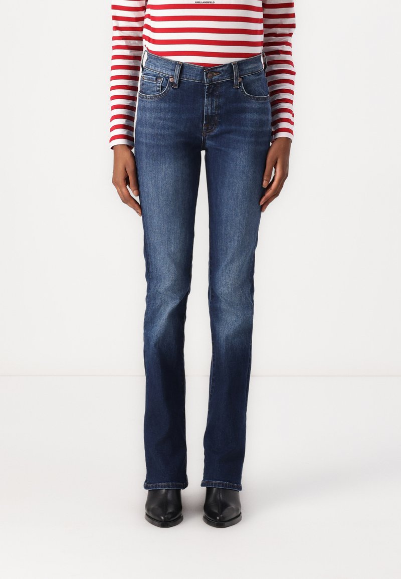 Blue denim jeans with a slim fit, flared leg, five-pocket design, and contrasting stitching. Worn with black ankle boots.