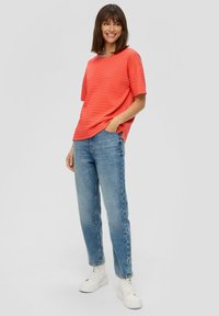 Koralen textuur katoen t-shirt met korte mouwen, gecombineerd met lichtblauwe hoge jeans en witte platform sneakers.
