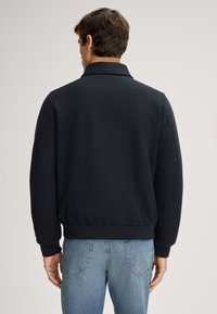 Marineblauwe fleece bomberjack met een kraag, ribgebreide manchetten en band. Zachte textuur met een ontspannen pasvorm, gecombineerd met lichtblauwe jeans.