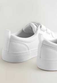 Vita sneakers med en slät syntetisk ovandel, texturerade detaljer, rund form, vadderad krage och en platt gummisula. Kardborrestängning.