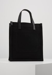 Černá plátěná taška přes rameno s koženými uchy, obdélníkový tvar, s přední kapsou a šitými detaily. Odolný materiál a elegantní design.