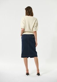 Cremefarvet strikket sweater med korte puffærmer, kombineret med en mørkeblå denim blyantskirt med baglomme og kontraststing.