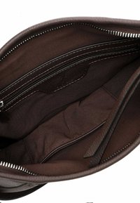 Interno di una borsa a tracolla in pelle marrone, con una fodera in tessuto morbido, tasca con zip e dettagli in pelle. Chiusura con zip e cuciture bianche.