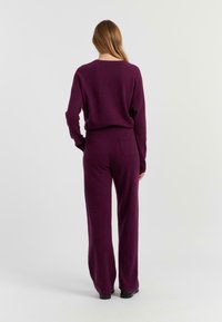 Paarse gebreide twee-delige set met een relaxte pasvorm, lange mouwen en wijde broekspijpen. Achterzakdetail op de broek. Gladde textuur.