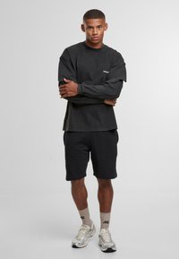 Czarna koszula z długim rękawem w połączeniu z ciemnymi szortami. Materiał wygląda na miękki. Koszula ma małe logo na piersi. Buty są srebrne z białymi akcentami.