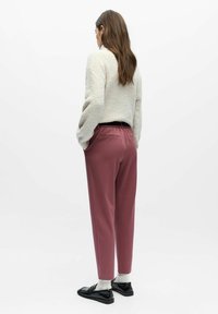 Lys grå, strukturert genser kombinert med høytlivede, rosenrøde bukser. Sorte slip-on sko og hvite sokker fullfører antrekket.