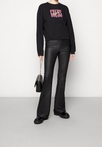 Svart kortad sweatshirt med rosa och gula "GUESS"-logotypen, kombinerad med svarta utsvängda byxor i konstläder och kraftiga svarta plattformsskor.