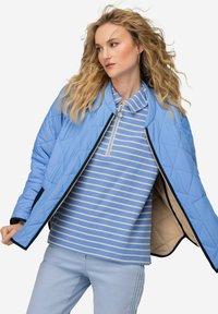 Světlomodrá prošívaná bunda s námořnickými akcenty, se zipem vpředu a kulatým límcem, nošená přes modro-béžovou pruhovanou košili a světlými kalhotami.