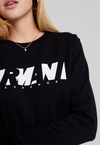 Svart sweatshirt med vit grafiktext "ARMANI EXCHANGE." Långa ärmar, rund halsringning med en mjuk textur.