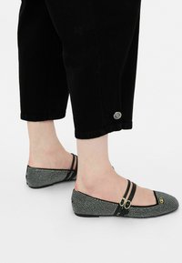 Pantofi plata negri și albi cu un superior texturat și cu model, având două curele negre și accente din metal aurit.