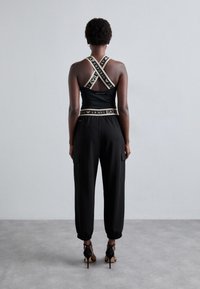 Melna sporta topiņš ar krustveida siksnām, apvienots ar melnām treniņu biksēm, kas aprīkotas ar kabatām un pieguļošām aprocēm, valkāts ar papēžiem.