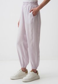 Helle lavendel Jogginghosen mit elastischem Bund, seitlichen Taschen und schmal zulaufenden Bündchen, kombiniert mit weißen Turnschuhen mit beigem Akzent.